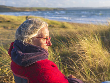 Ältere Frau sitzt an einem sonnigen Tag im Gras in Sainte-Anne la Palud - LAF02647