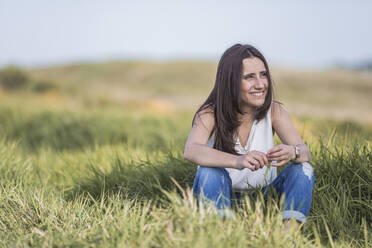 Schöne junge Frau, die wegschaut, während sie inmitten von Gras sitzt - SNF01026