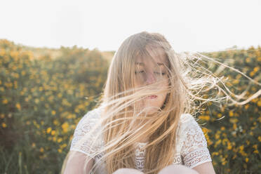 Der Wind bläst das Haar einer jungen Frau, die auf einem landwirtschaftlichen Feld sitzt - SNF01030