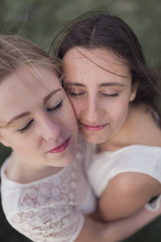 Beautiful female friends with eyes closed embracing each other stock photo