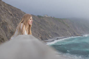 Schöne blonde Frau, die auf das Meer blickt, während sie am Beobachtungspunkt steht - SNF01040