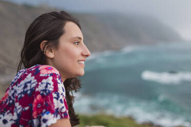 Lächelnde junge Frau genießt die Aussicht auf das Meer im Urlaub - SNF01042