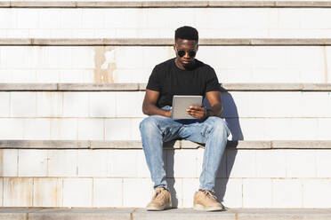 Young man using digital tablet while sitting on steps during sunny day - PNAF00580