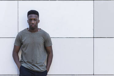 Young man with hands in pockets standing against white wall - PNAF00585