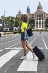 Female tourist crossing road with suitcase on street at city - PNAF00597