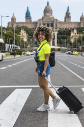 Smiling female wheeling luggage while walking on street at city - PNAF00598
