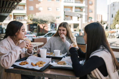 Female friends having fast food at outdoor restaurant - GRCF00631