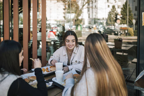 Weibliche Freunde unterhalten sich bei einem schnellen Essen in einem Restaurant im Freien - GRCF00632