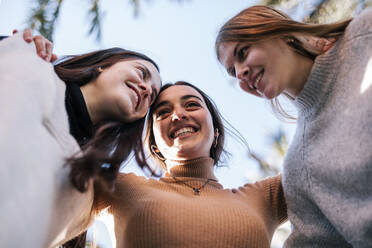 Lächelnde Freundinnen im Teenageralter, die sich im Park an den klaren Himmel kuscheln - GRCF00655