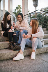 Female friends talking while eating ice cream on steps - GRCF00664