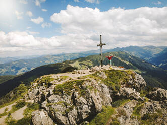 Drohnenaufnahme einer Frau auf einem Berggipfel vor bewölktem Himmel - PSIF00418