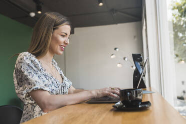 Lächelnde Geschäftsfrau arbeitet an einem Laptop auf einem Tisch in einem Café - DSIF00277