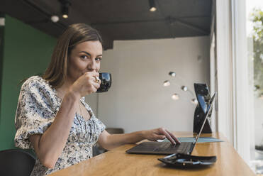 Businesswoman drinking coffee while using laptop on table in coffee shop - DSIF00278