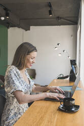 Fröhliche Geschäftsfrau arbeitet an einem Laptop auf einem Tisch in einem Café - DSIF00279