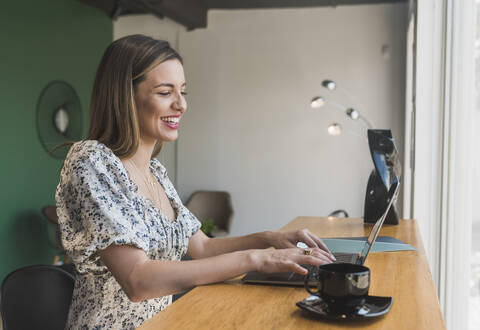 Fröhliche Unternehmerin bei der Arbeit am Laptop auf dem Tisch im Restaurant, lizenzfreies Stockfoto