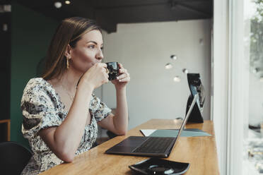 Geschäftsfrau mit Laptop auf dem Tisch, die Kaffee trinkt, während sie in einem Café sitzt - DSIF00283