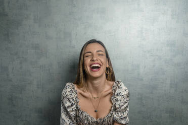 Schöne Frau lachend beim Sitzen gegen eine Betonwand - DSIF00290