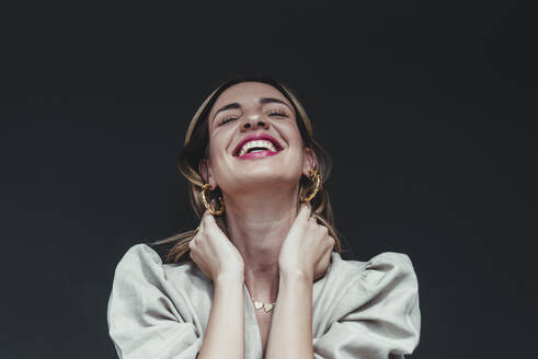 Cheerful woman with hands in hair against black background - DSIF00304