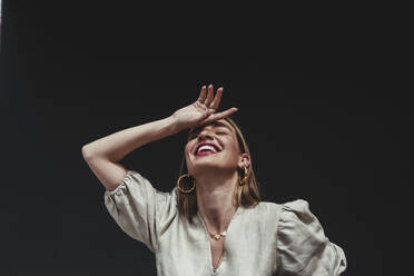 Fröhliche Frau mit Hand auf dem Kopf vor schwarzem Hintergrund - DSIF00307