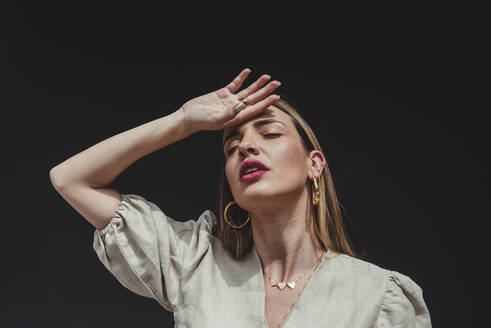 Close-up of beautiful woman with eyes closed and hand on head against black background - DSIF00308