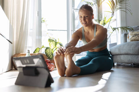 Frau mit digitalem Tablet beim Dehnen während des Trainings zu Hause, lizenzfreies Stockfoto