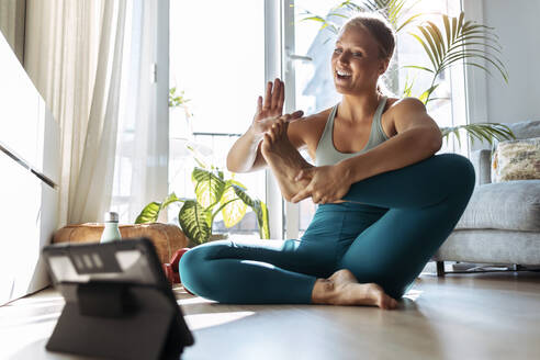 Lächelnde Frau, die Yoga macht, während sie zu Hause über ein digitales Tablet lernt - JSRF01272