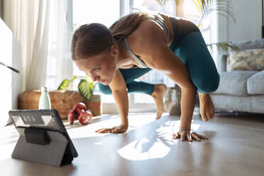Junge Frau benutzt ein digitales Tablet, während sie zu Hause Handstand-Yoga macht - JSRF01276