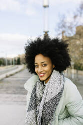 Lächelnde Afro-Frau mit Händen in den Taschen, die im Winter im Freien steht - XLGF01030