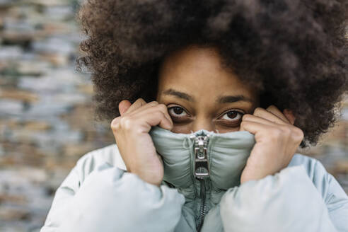 Afro young woman holding winter coat on face outdoors - XLGF01033