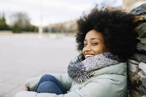 Smiling young woman in warm clothing while sitting outdoors - XLGF01034