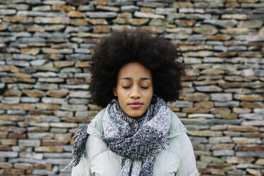 Afro junge Frau mit geschlossenen Augen gegen Steinwand im Winter - XLGF01035