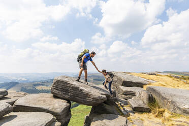 Männlicher Wanderer, der seiner Freundin beim Bergsteigen in den Ferien hilft, an einem sonnigen Tag - WPEF03966