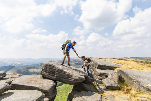 Männlicher Wanderer, der seiner Freundin beim Bergsteigen in den Ferien hilft, an einem sonnigen Tag - WPEF03966