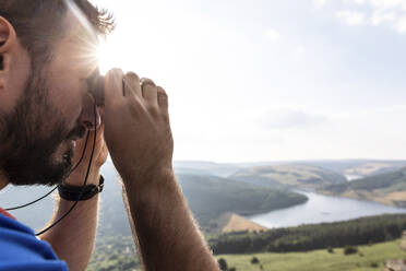 Junger Mann betrachtet die Aussicht durch ein Fernglas im Sonnenlicht während der Ferien - WPEF03972