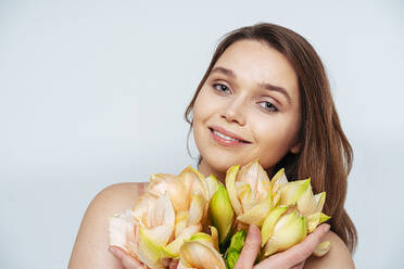 Young woman with flowers smiling while standing against white background - OIPF00158