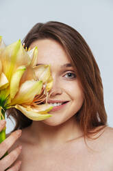 Smiling woman covering face with bunch of flowers while standing against white background - OIPF00160