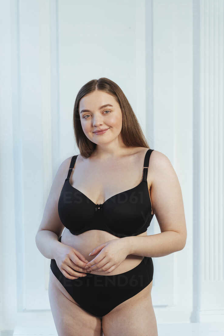 Beautiful plus size model in lingerie standing against white wall