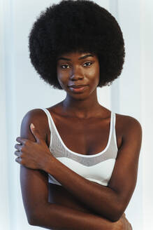 Afro-Model in weißen Dessous umarmt sich selbst, während sie gegen eine weiße Wand steht - OIPF00199