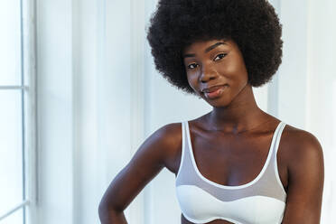 Smiling young female model in lingerie standing against white wall - OIPF00202