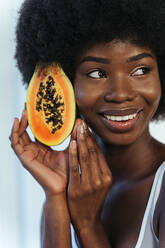 Lächelndes weibliches Modell, das wegschaut, während es eine Papaya am Gesicht hält - OIPF00208