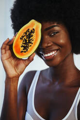 Lächelndes weibliches Modell in weißem BH, das seine Augen mit einer Papayascheibe bedeckt - OIPF00210
