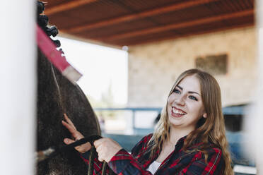 Cheerful young woman with horse at farm - MRRF00833
