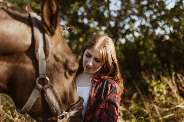 Junge Frauen betrachten ein Pferd auf einem Bauernhof an einem sonnigen Tag - MRRF00838