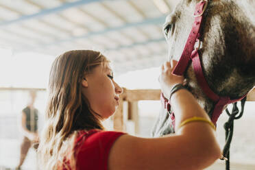 Junge Frau streichelt Pferd mit Zuneigung auf dem Bauernhof - MRRF00840
