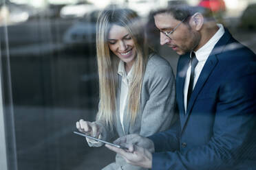 Businessman having discussion over digital tablet with colleague while standing in office - JSRF01280