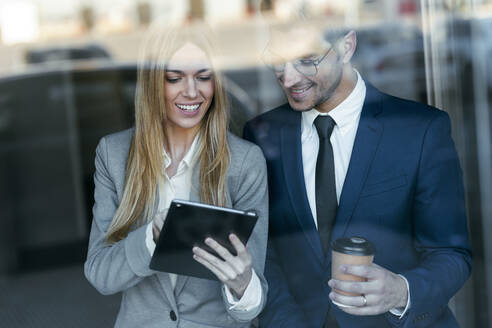 Lächelnde Geschäftsfrau, die mit einem Kollegen über einem digitalen Tablet arbeitet, während sie im Büro steht - JSRF01282