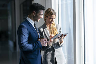 Businesswoman smiling while using digital tablet standing by colleague in office - JSRF01289