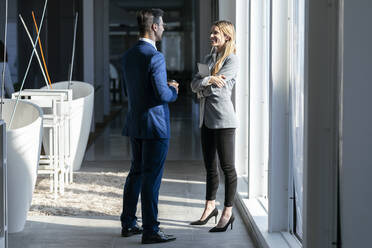 Smiling businesswoman talking to colleague while standing in office - JSRF01290