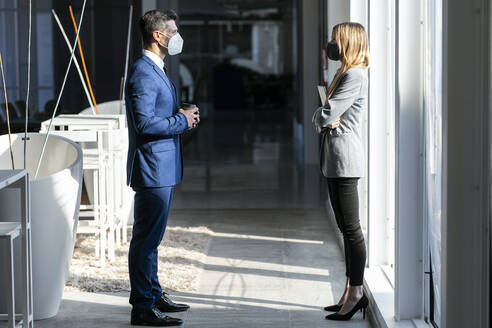 Business people wearing protective face mask standing at social distance while working in office during COVID-19 - JSRF01292