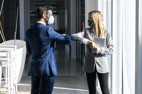 Businessman giving elbow bump to colleague while standing in office during COVID-19 - JSRF01293